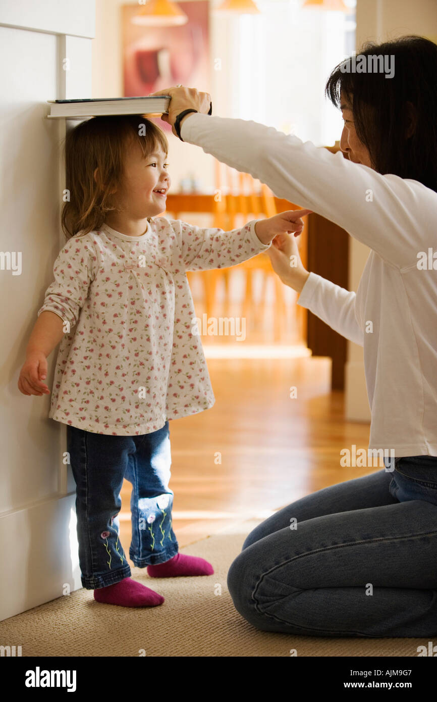 Asian measing madre la sua giovane figlia altezza contro una porta a casa Foto Stock
