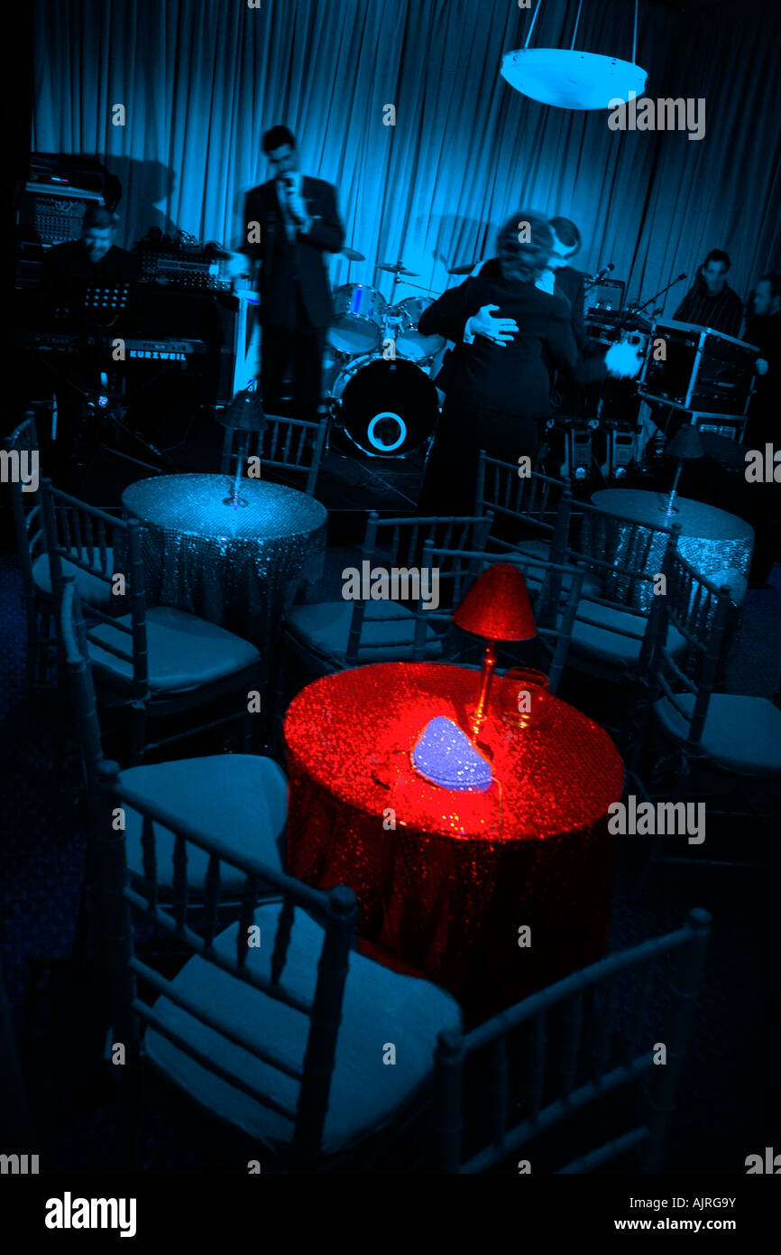 Discoteca scena, tavoli e sedie, sala blu con la tabella evidenziata in rosso la luce. Il cantante e una singola coppia danzante. Aspetto datato Foto Stock