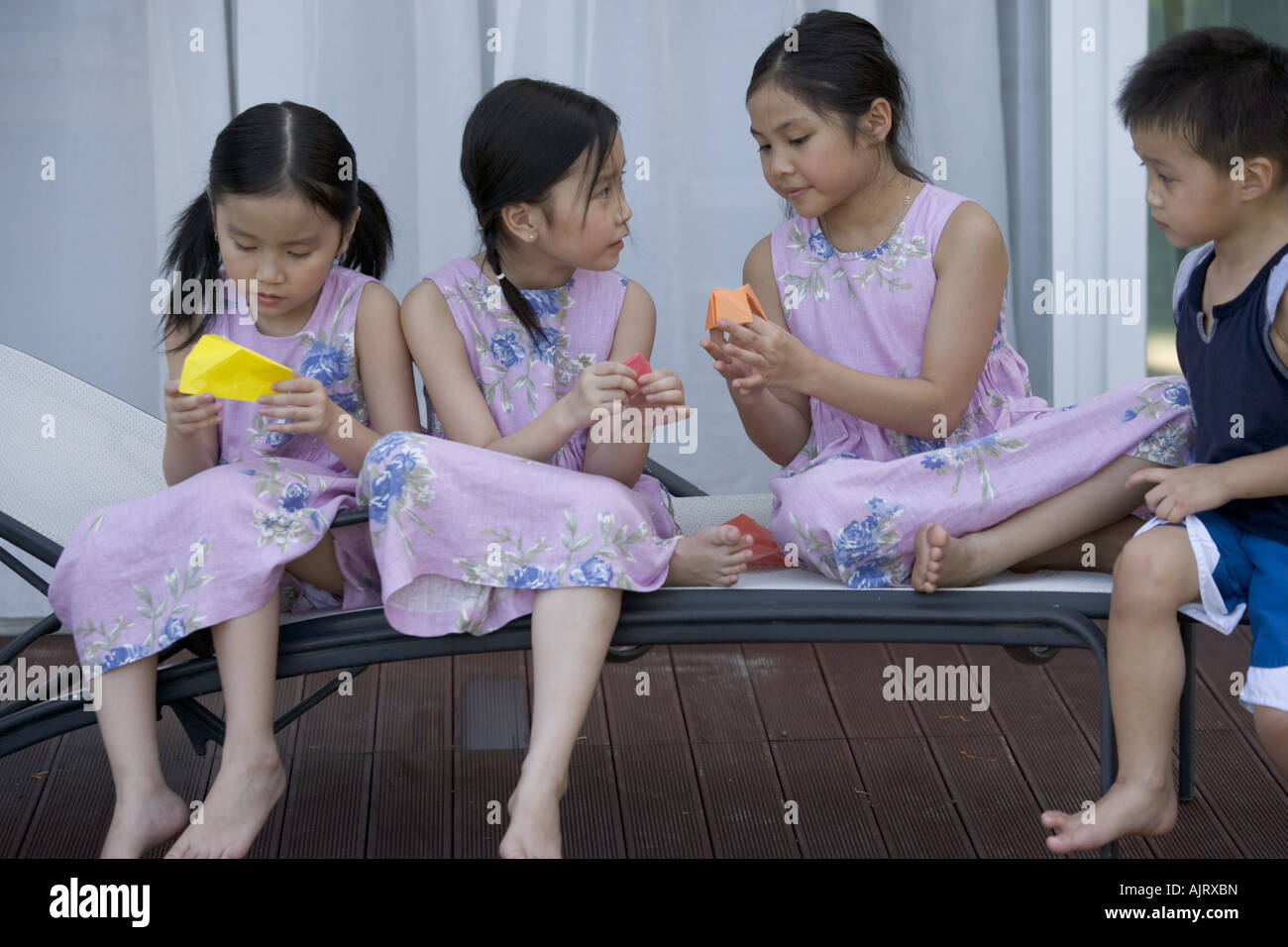 Le tre ragazze fare carta barche con un ragazzo seduto accanto a loro. Foto Stock