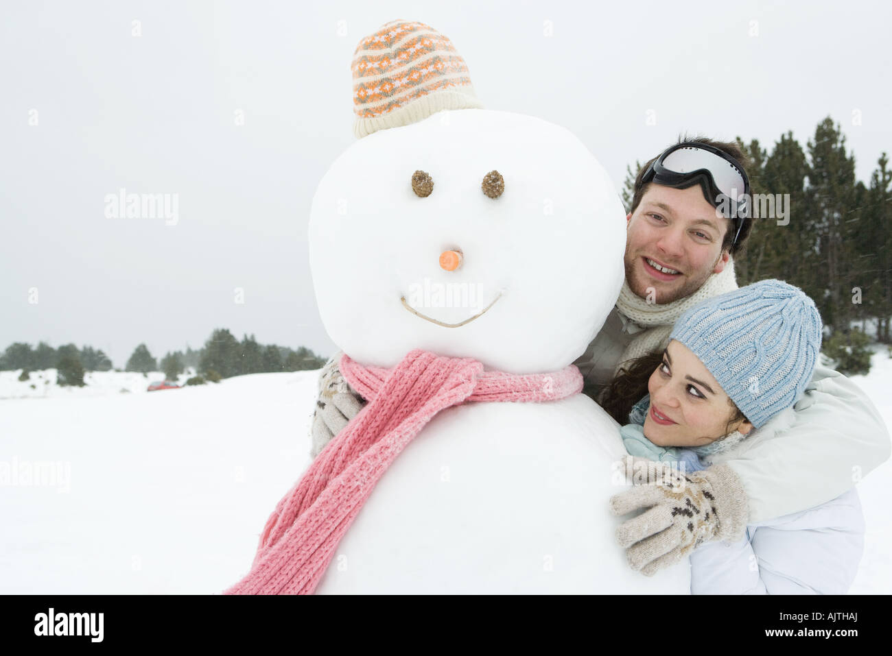 Due giovani amici in piedi con pupazzo di neve, entrambi sorridenti, uno che guarda in telecamera Foto Stock
