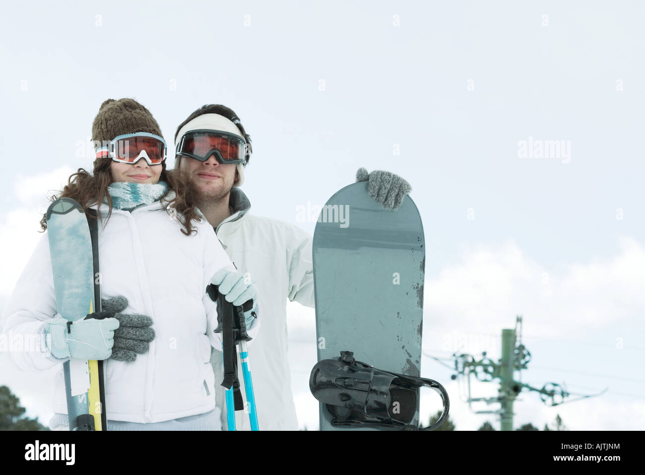 Coppia giovane vestito di usura di sci, uomo con lo snowboard, donna azienda bastoni da sci Foto Stock