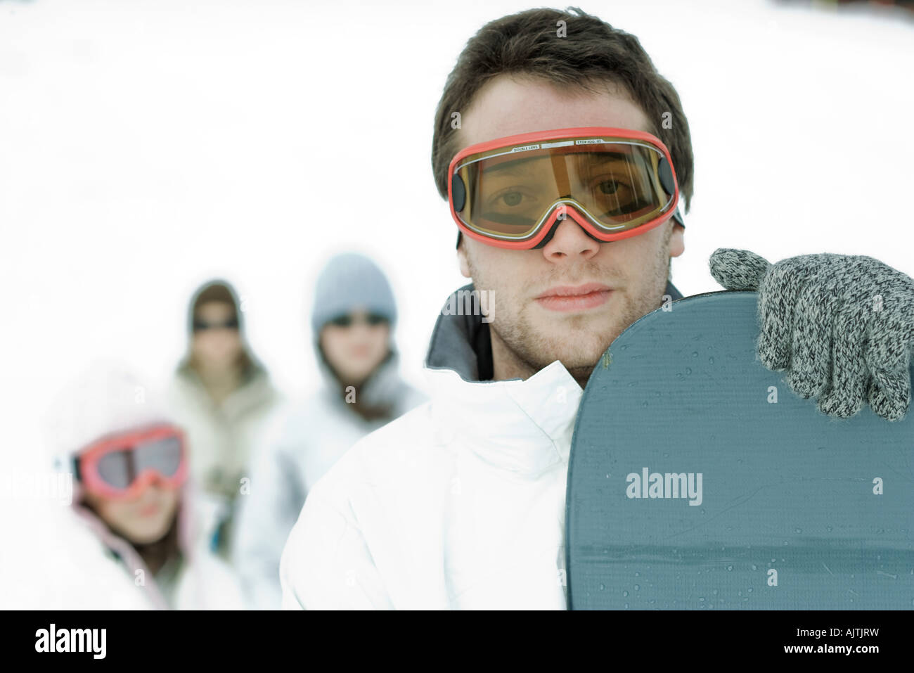 Giovane maschio snowboarder guardando la telecamera, amici in piedi in background, ritratto Foto Stock