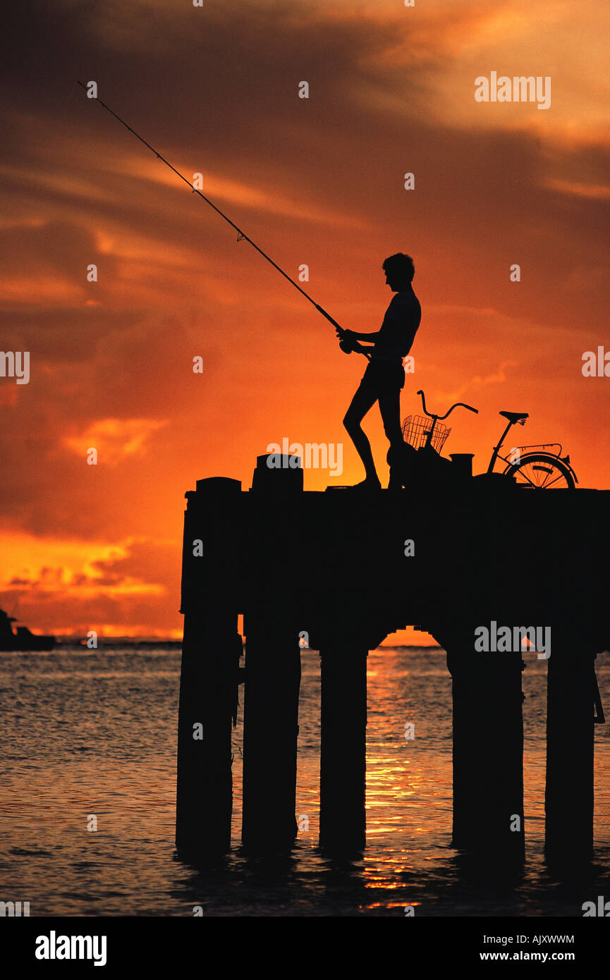 Silhouette di giovane che pesca dal molo al tramonto. Australia. Foto Stock