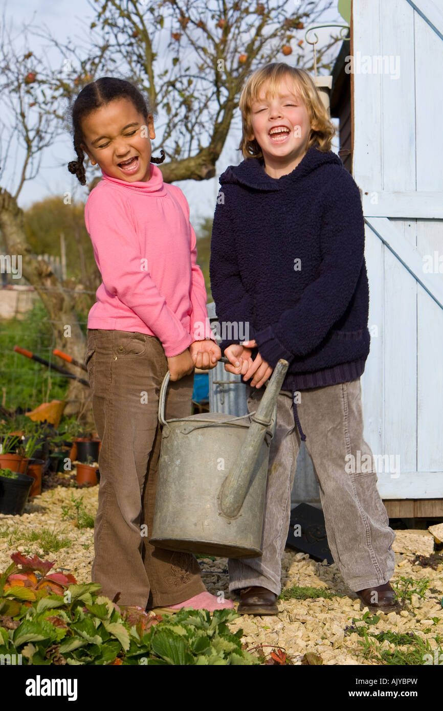 Due giovani bambini che portano una pesante annaffiatoio in un giardino autunnale Foto Stock