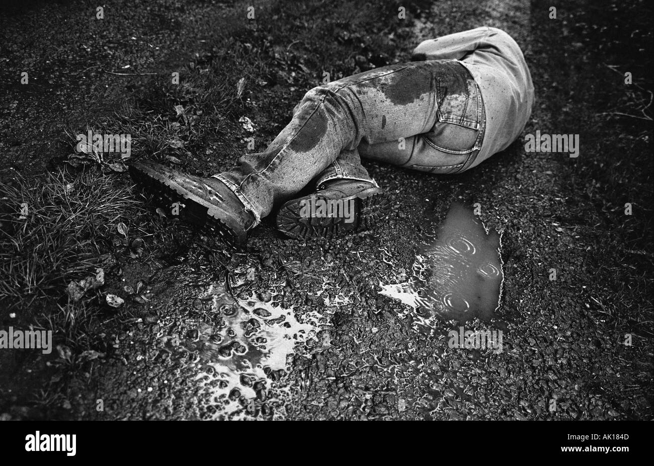 Mans corpo disteso su terreni fangosi strada bagnata Foto Stock