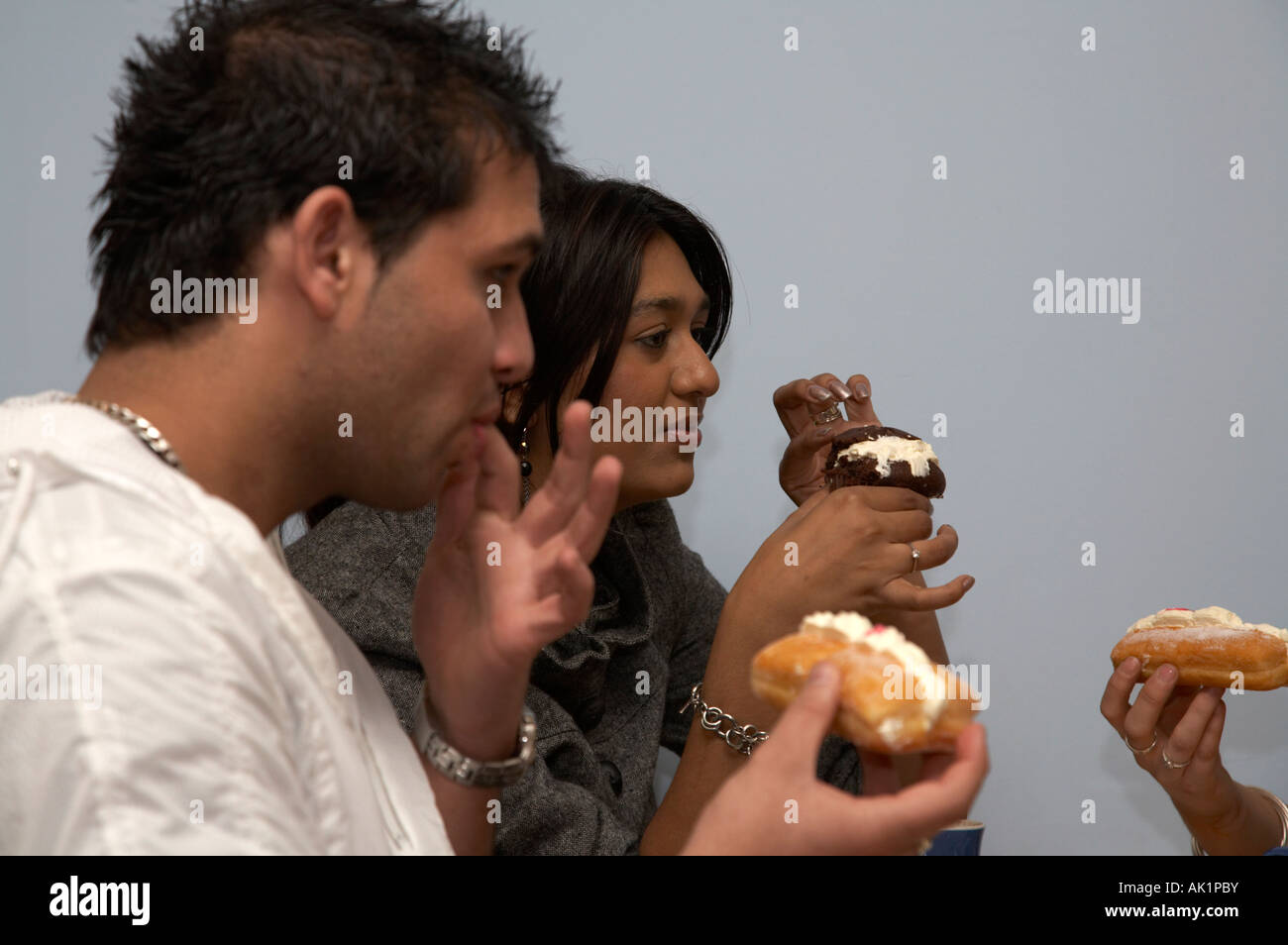 Due studenti asiatici che mangiare pasticcini e muffin in un caffè con gli amici Foto Stock
