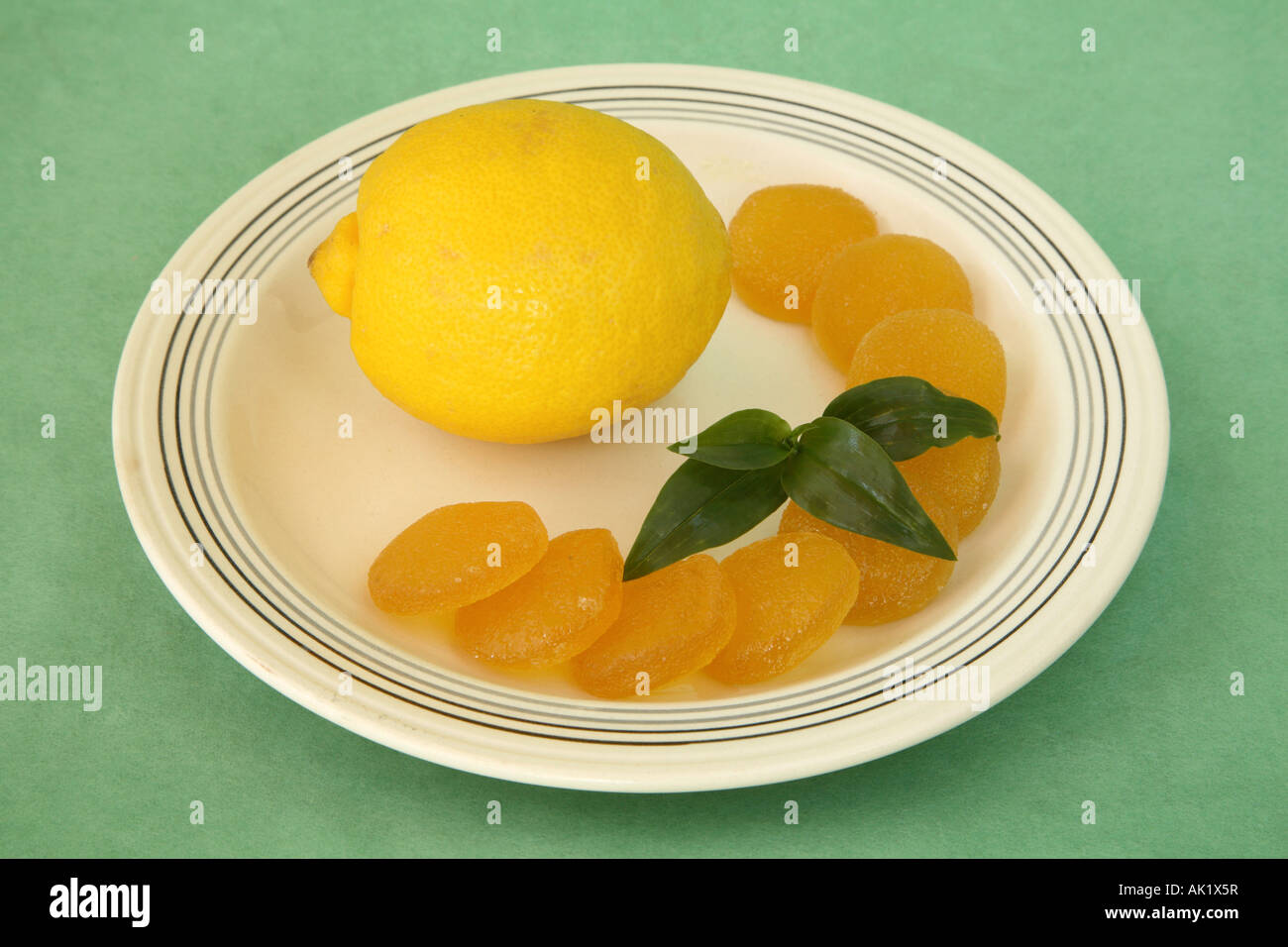 Limone giallo su una piastra con una mezzaluna di circolare di gelatina di Limoni canditi in arco sulla destra con un pezzo di verde Foto Stock