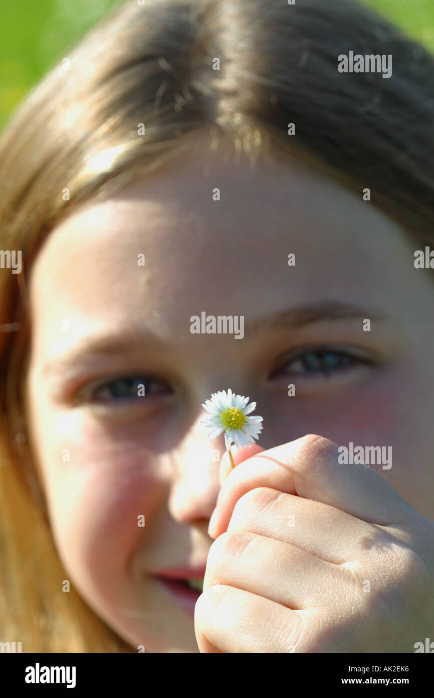 Ragazza giovane di età compresa tra 12 anni in possesso di un piccolo fiore a margherita davanti al suo volto sorridente Foto Stock