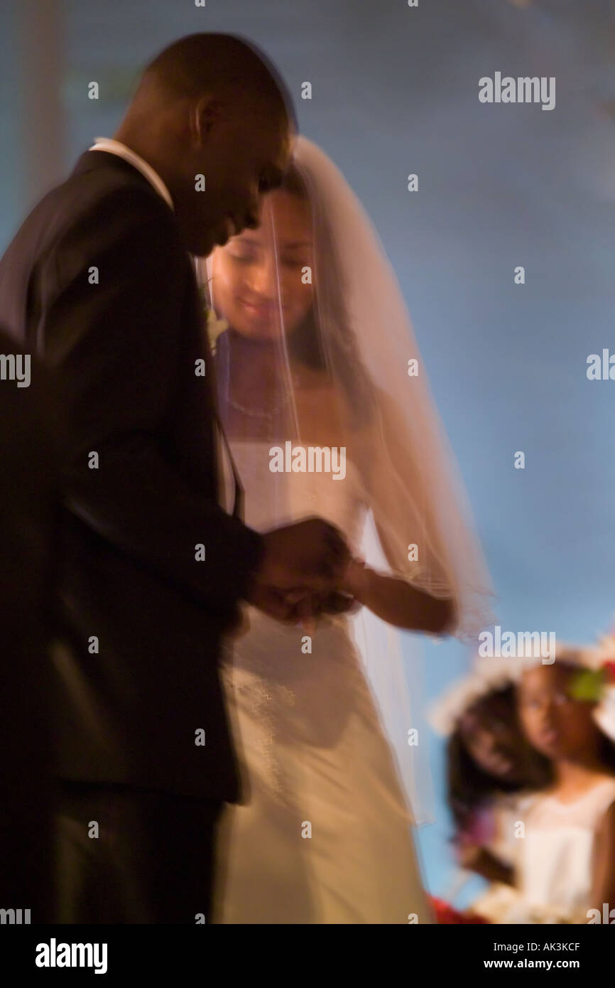 Una razza mista sposa sguardi al suo americano africano sposo di mettere l'anello sul suo dito durante il loro matrimonio in Santa Ana CA Foto Stock