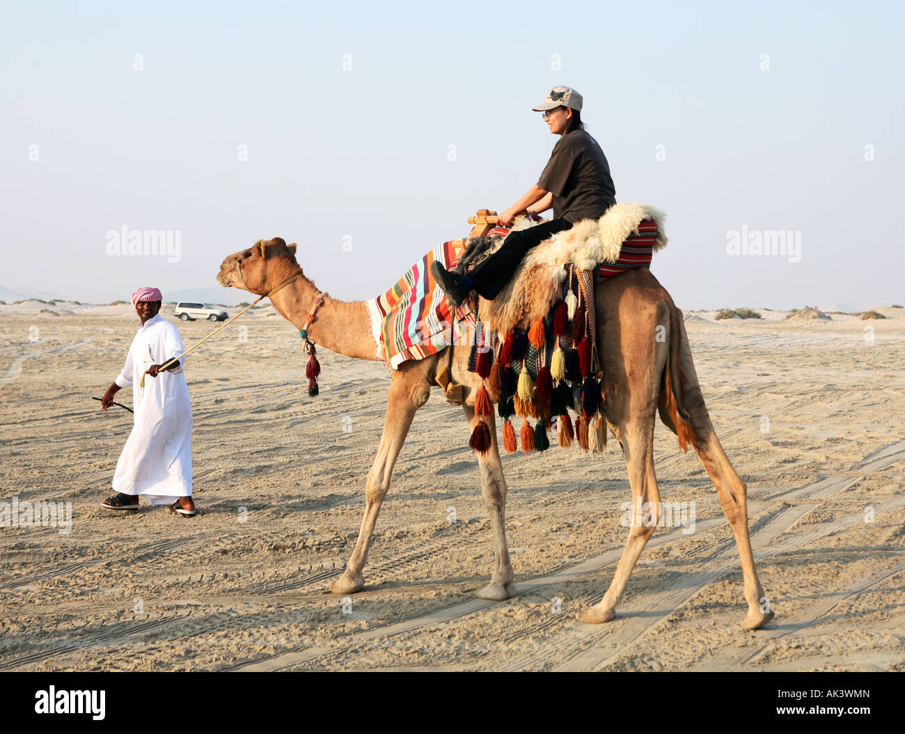 Un espatriato giapponese donna Cavalca un cammello guidato da un beduino nel deserto Qatar accanto alla Sealine Beach Resort Novembre 2007 Foto Stock