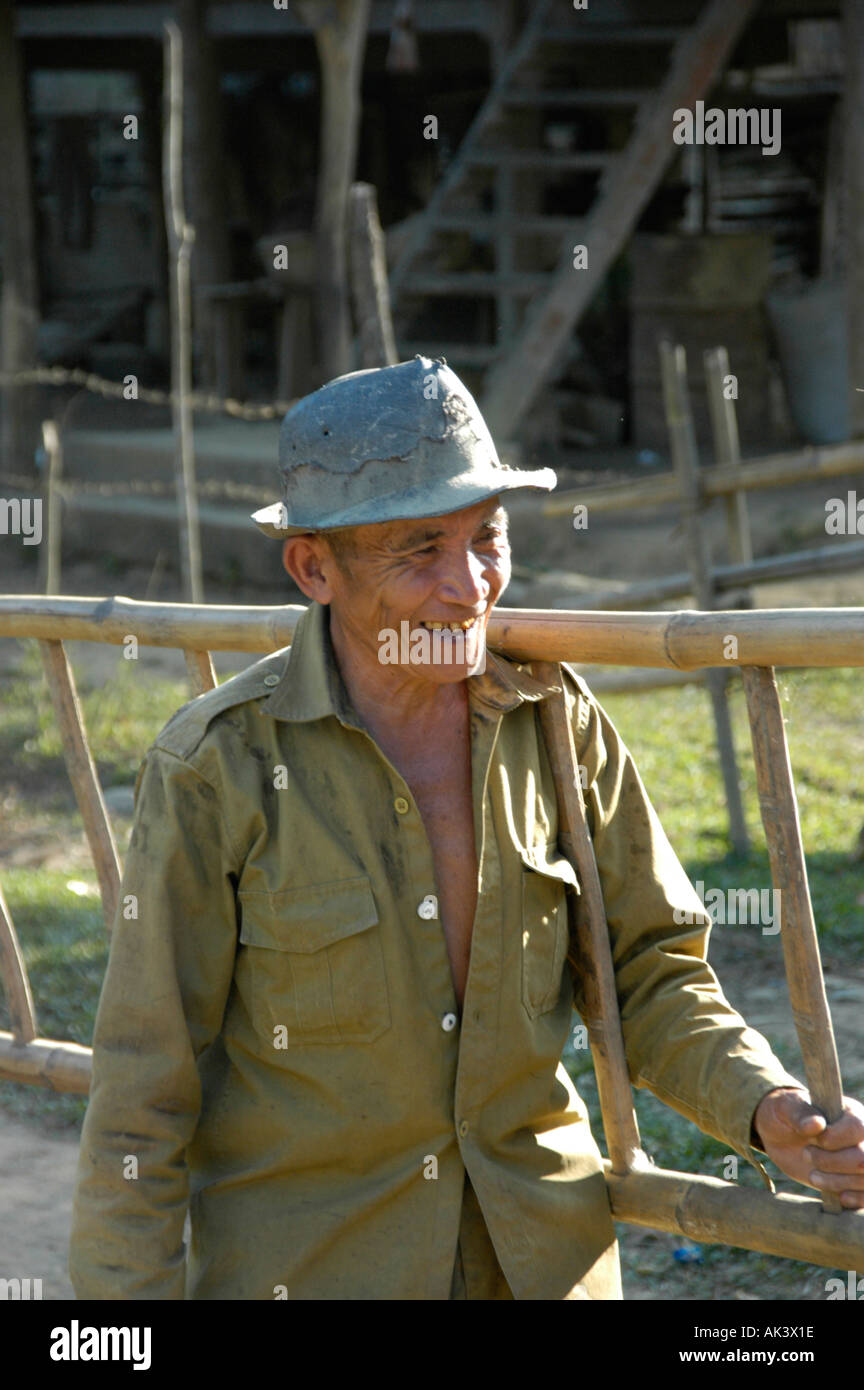 Uomo sorridente indossando un cappello che porta una scaletta di bambù vicino a Vang Vieng Laos Foto Stock
