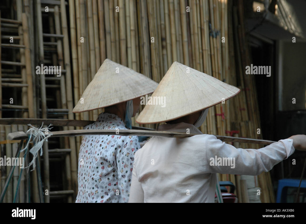 Due donne che indossano un cono a forma di cappello a piedi lungo le scale di bambù nella città vecchia di Hanoi Vietnam Foto Stock
