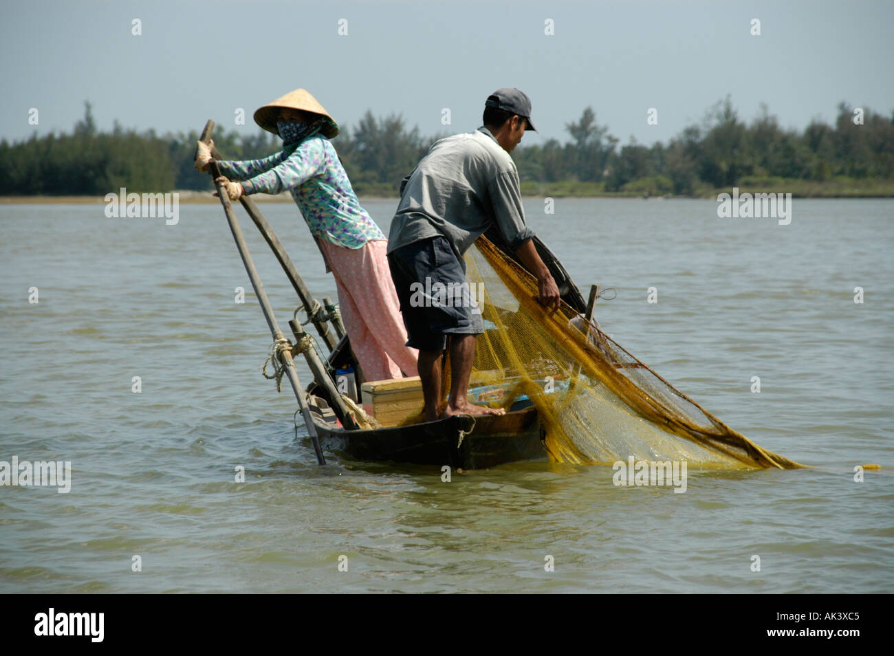 Fisherman ottiene il net mentre sua moglie guida l'imbarcazione inclinato Hoi An Vietnam Foto Stock