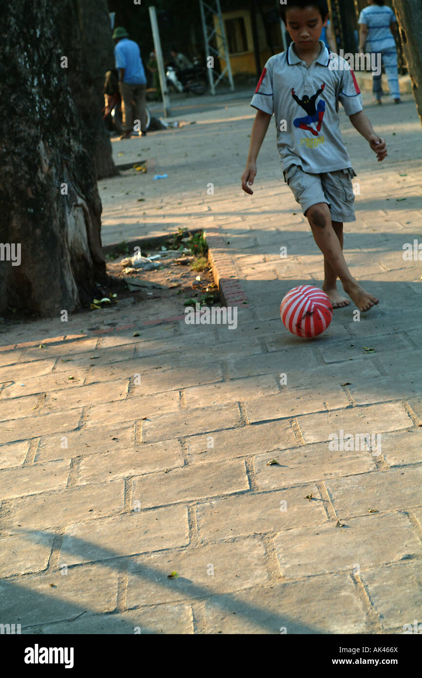 Un giovane ragazzo butta un calcio come il sole tramonta ad Hanoi Vietnam Foto Stock