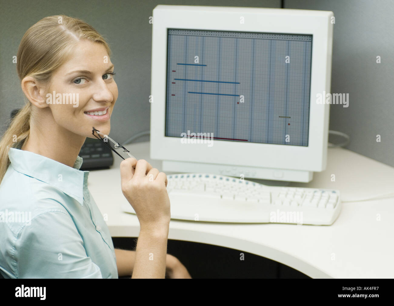 Femmina di lavoratore di ufficio seduti al computer, sorridente in telecamera Foto Stock