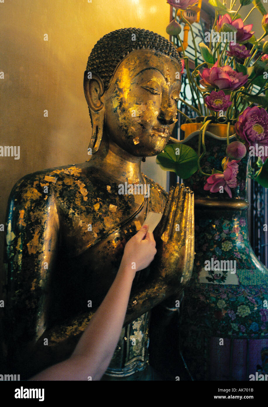 Al Wat Traimit, Bangkok, Thailandia - rendere merito mediante incollaggio di piccole parti di foglia oro di statue sacre Foto Stock