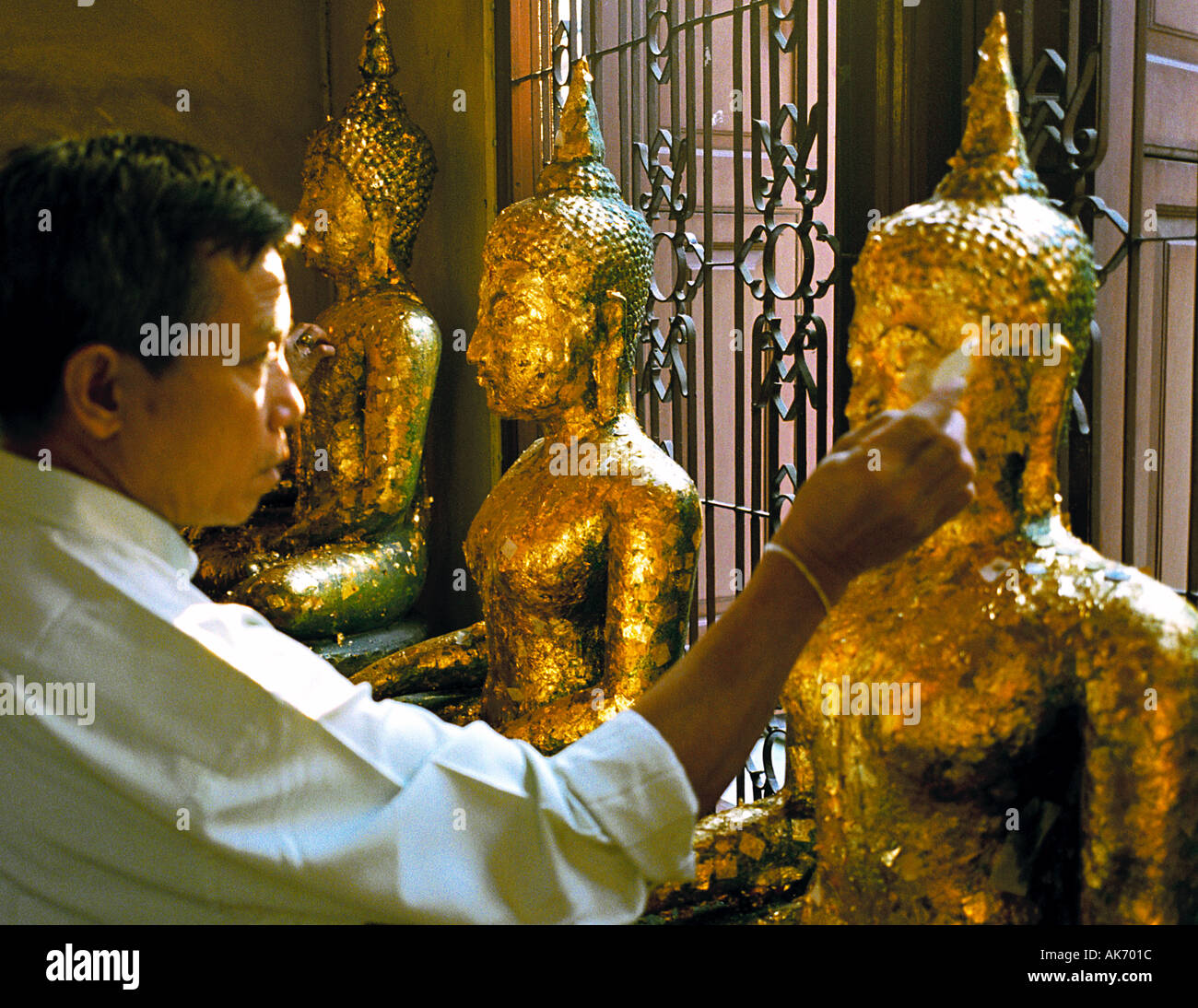 Al Wat Traimit, Bangkok, Thailandia - rendere merito mediante incollaggio di piccole parti di foglia oro di statue sacre Foto Stock
