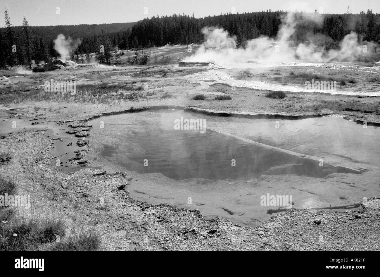 Piscina d'acqua calda e un geyser erutting sullo sfondo, Yellowstone National Park, Wyoming, USA. Sito patrimonio dell'umanità dell'UNESCO. Foto Stock