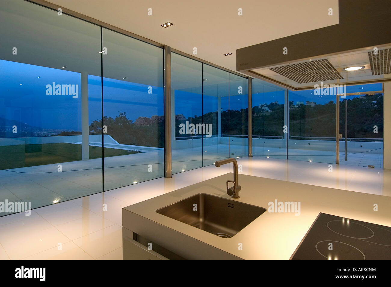 Lavandino in unità di isola in spagnolo moderno cucina con pareti in vetro e vista della terrazza di notte Foto Stock