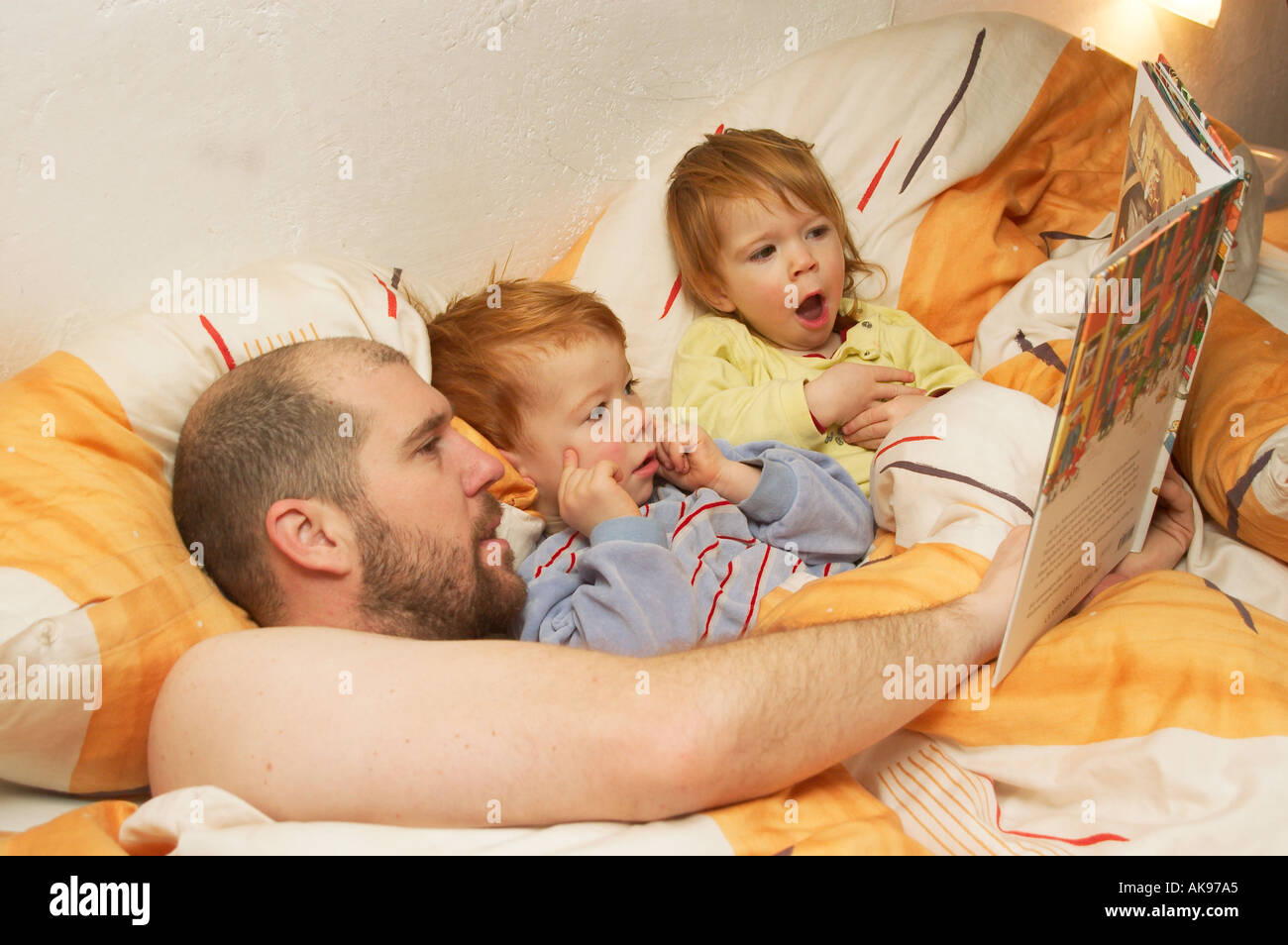 Padre con il suo bambino è la lettura di una buona storia di notte nel letto a leggere un libro MR Foto Stock