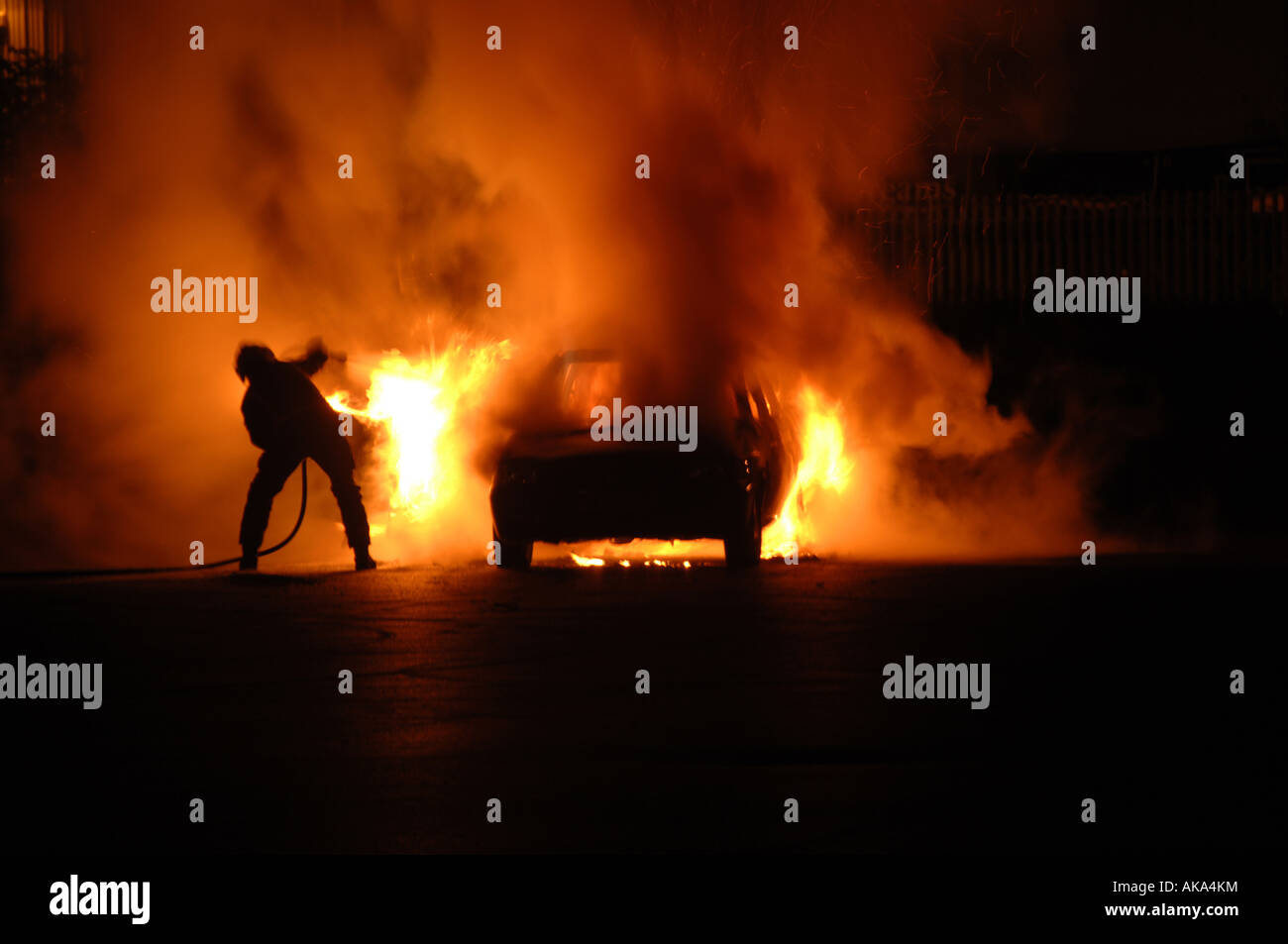 A fuoco singolo fighter battaglie da soli a mettere fuori fiammeggiante fuoco auto cercando di schivare il calore e nello stesso tempo compito suo tubo flessibile per acqua Foto Stock