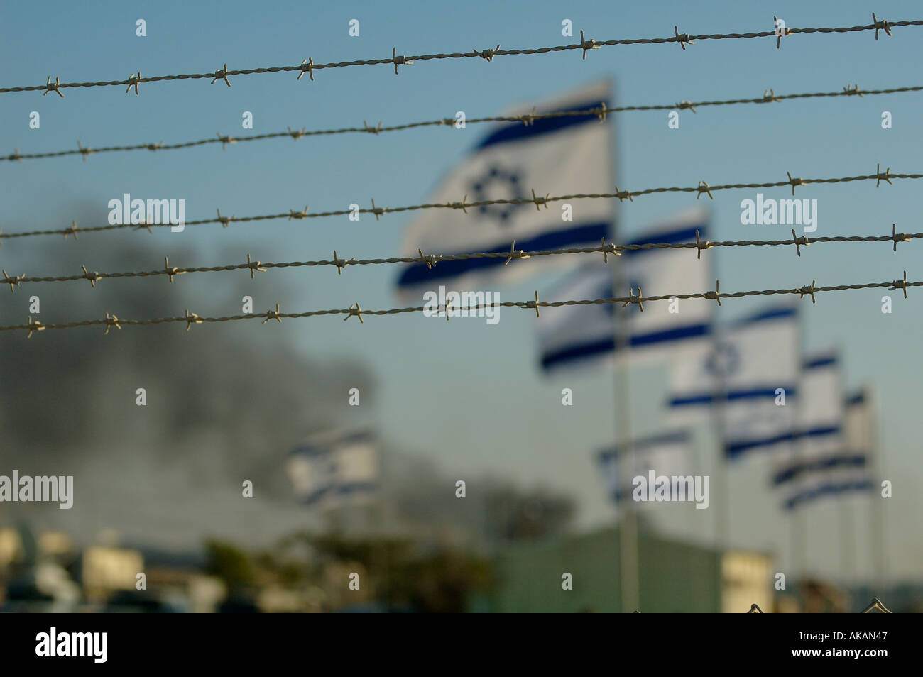 Fila di bandiere israeliane flutter in vento dietro al filo spinato con fumo pesante in background durante l insediamento ebraico evacuazione dalla striscia di Gaza Foto Stock