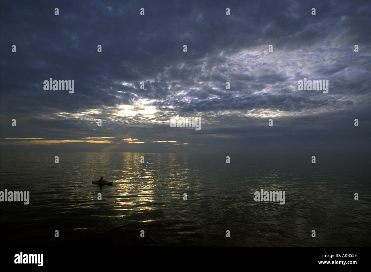 Una barca di solitario e fisherman si stagliano sotto un cielo drammatico e impostazione di ocean sun Foto Stock
