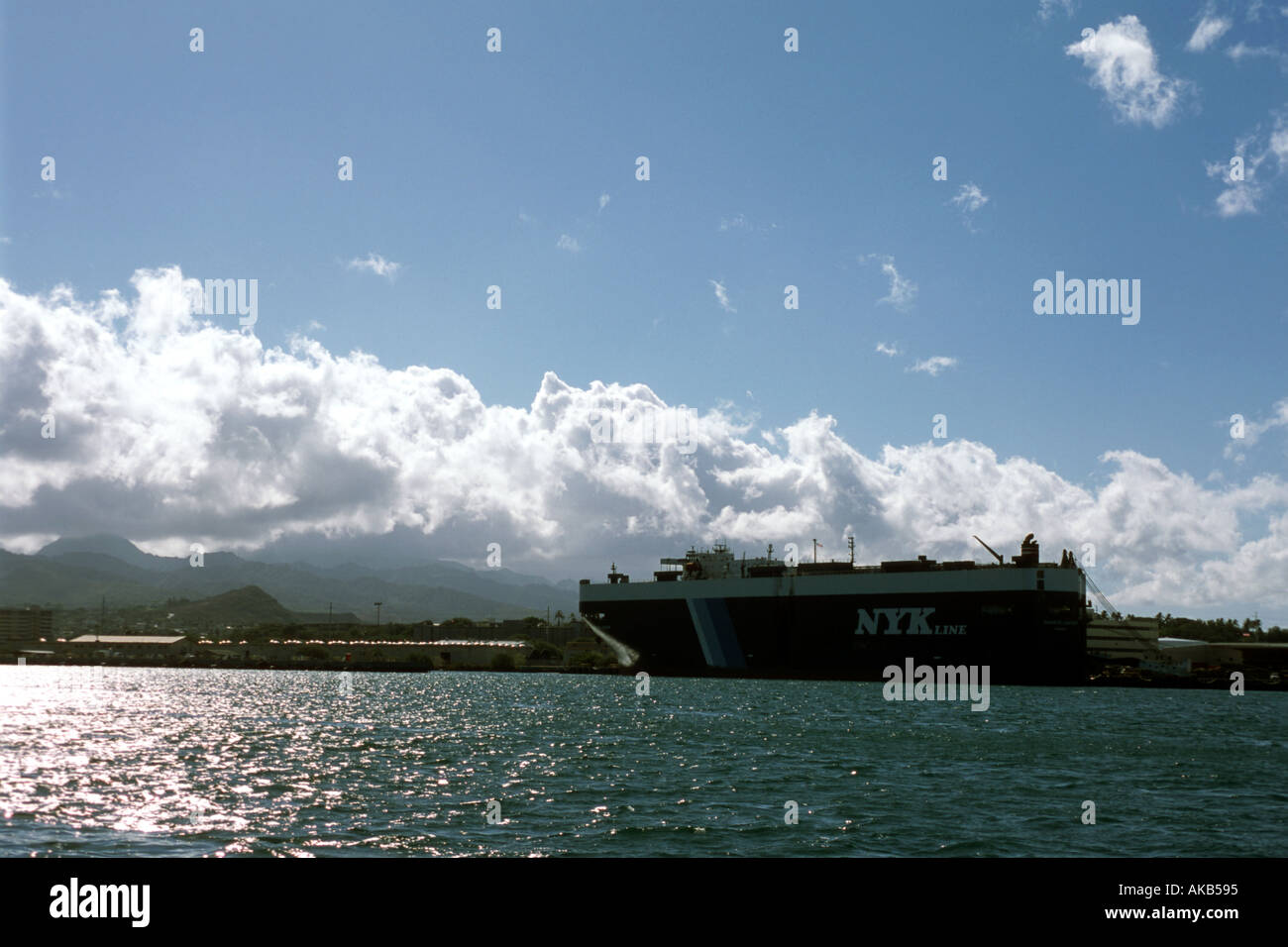 Un enorme nave mercantile liner riposa in un oceano porto contro un bianco brillante billowy cumulus nuvole e un cielo azzurro intenso Foto Stock