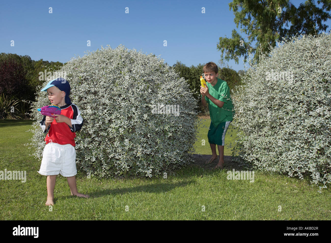 Due ragazzi (3-11) giocando con le pistole ad acqua tra boccole Foto Stock