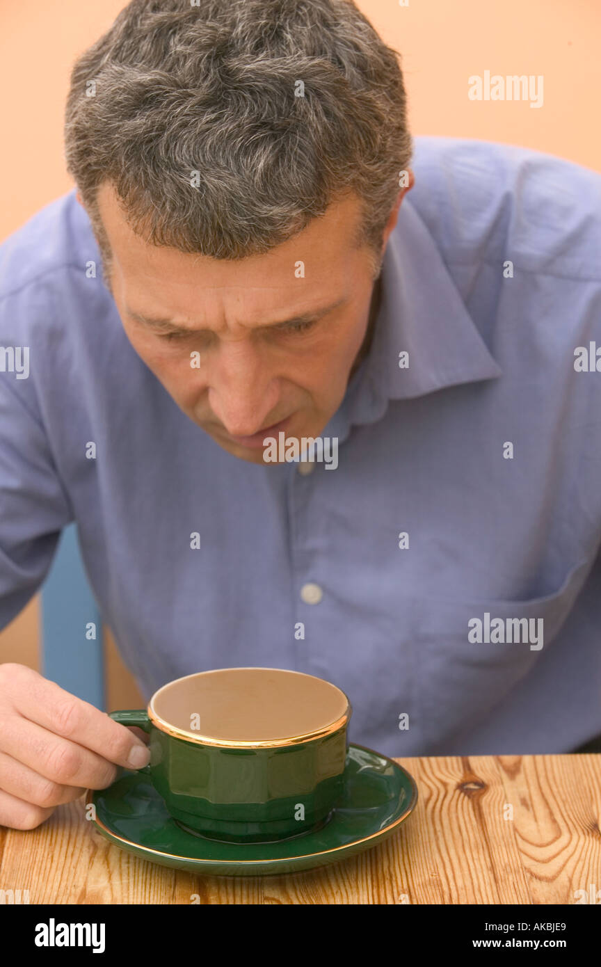 Uomo che guarda perplesso a una più piena tazza da caffè Foto Stock