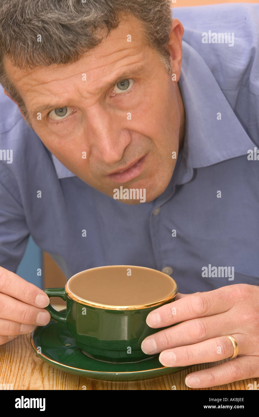Uomo che guarda perplesso a una più piena tazza da caffè Foto Stock