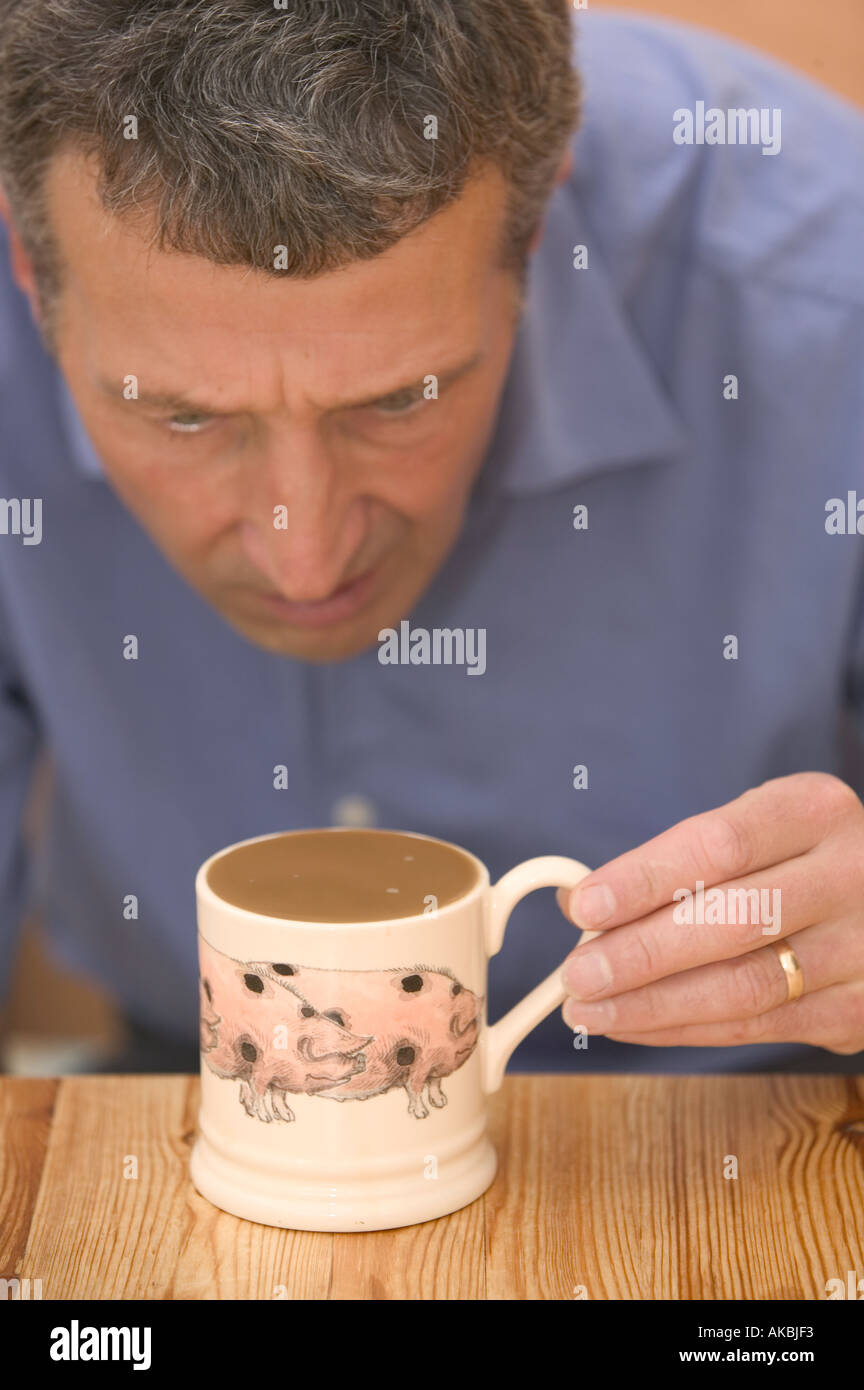 Uomo che guarda perplesso a una tazza piena di caffè Foto Stock