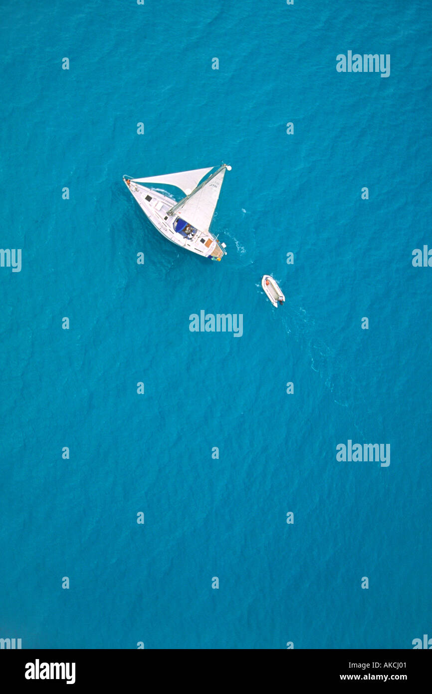 Uno yacht di traino di un dinghy vele nel mare dei Caraibi al largo della costa di antigua. Foto scattata da un elicottero. Foto Stock