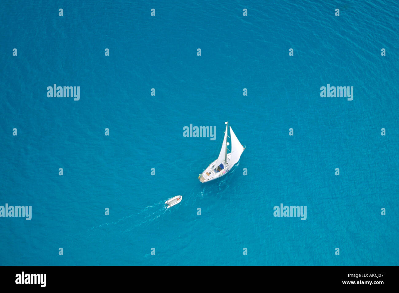 Uno yacht di traino di un dinghy vele nel mare dei Caraibi al largo della costa di antigua. Foto scattata da un elicottero. Foto Stock