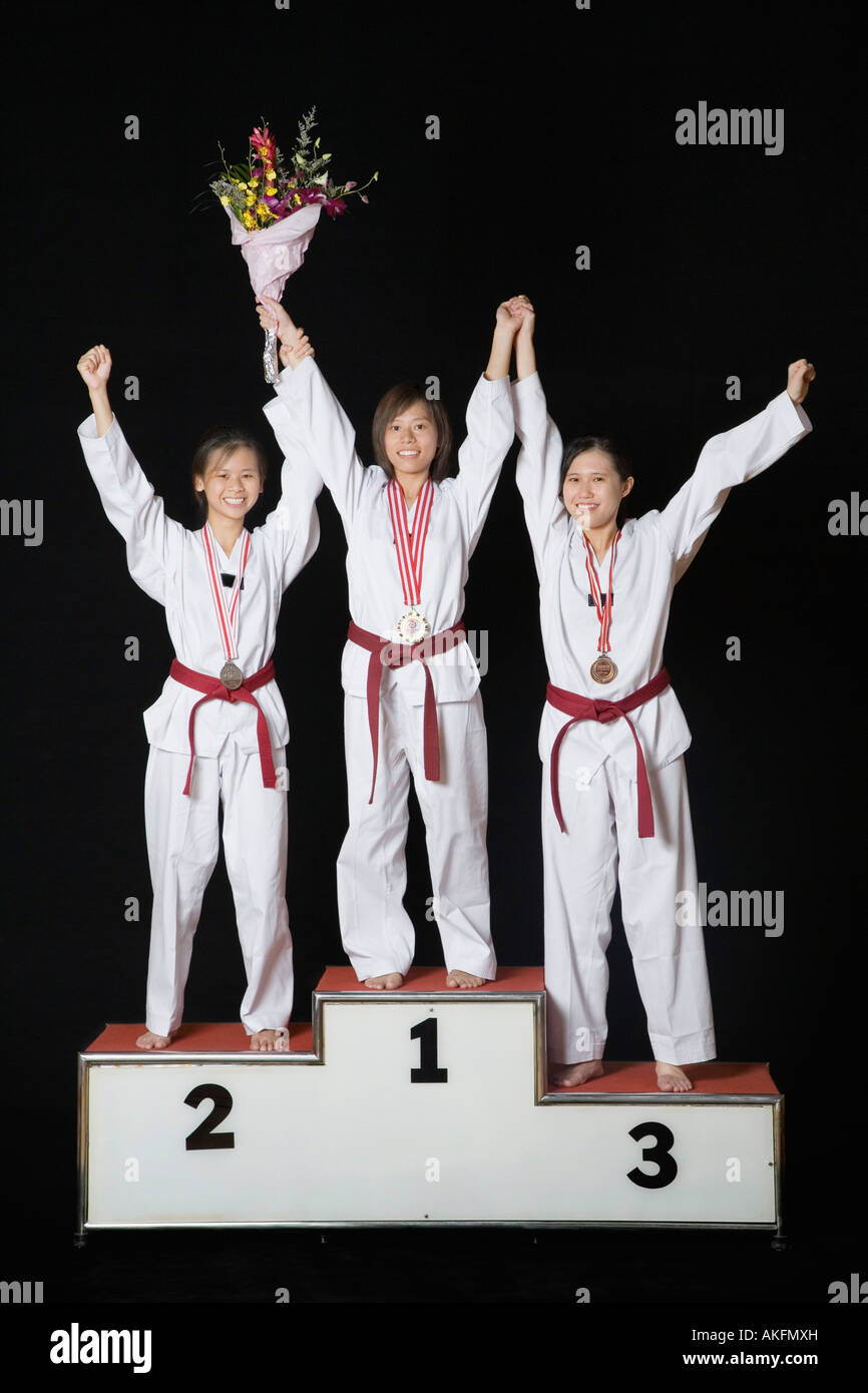 Tre giovani donne alzando le mani su un podio vincitori Foto Stock