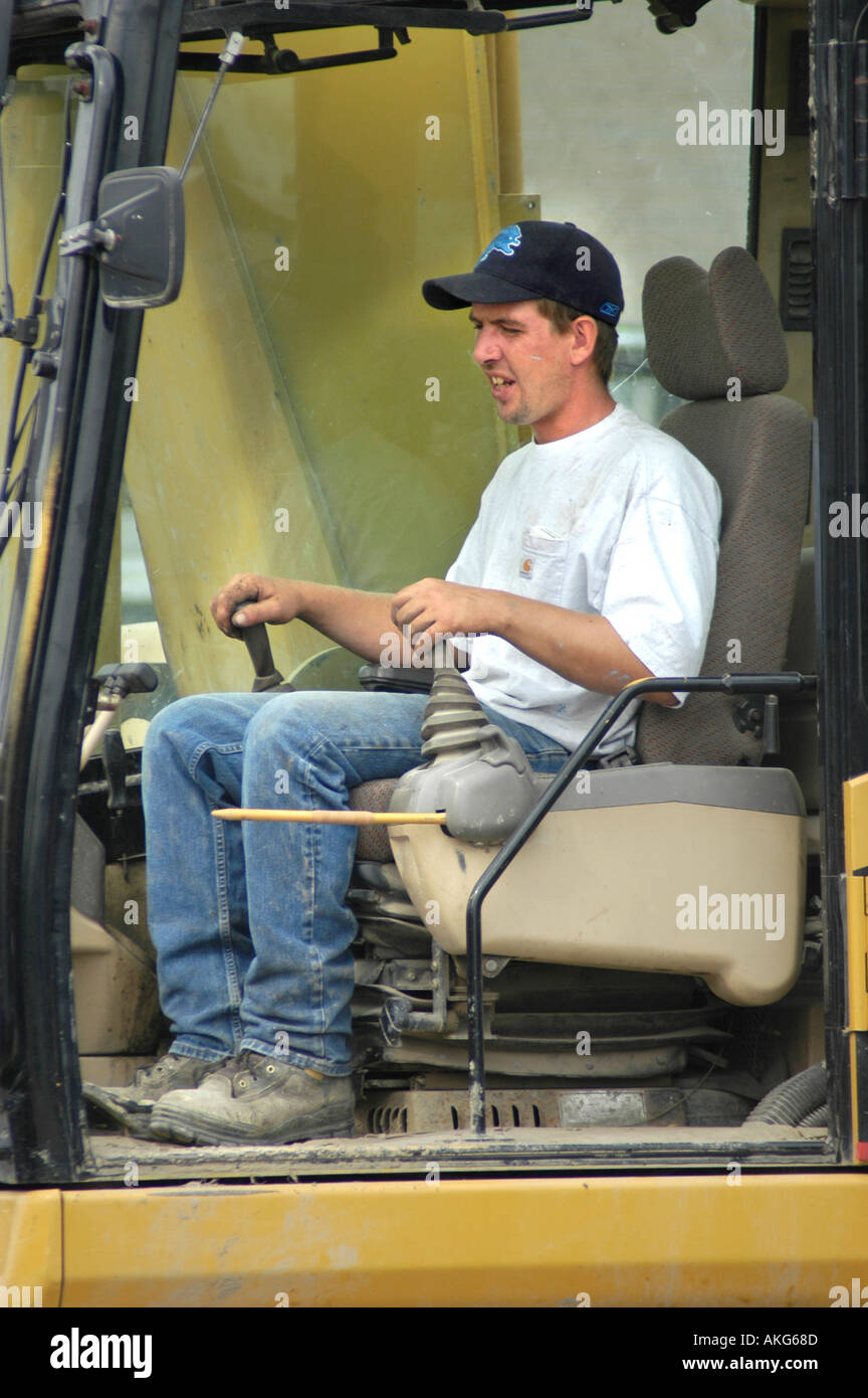 Uomo che lavora per abbattere il vecchio edificio del negozio per fare spazio a nuove utilizzando Caterpillar trattore utilizzando il joystick per il controllo Foto Stock