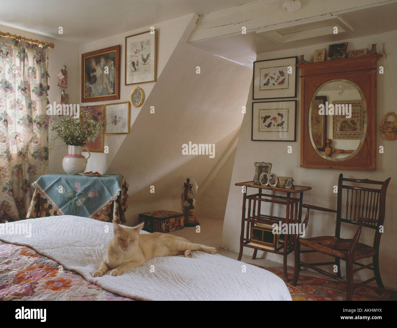 Gatto sul letto in camera da letto cottage con specchio antico e le immagini sulla parete Foto Stock