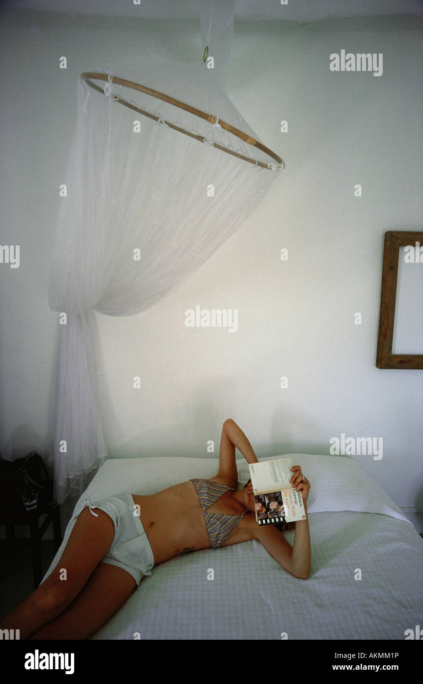 Ginostra Stromboli Sicilia una giovane donna posa su un letto di leggere un libro in un bianco lavato room Foto Stock
