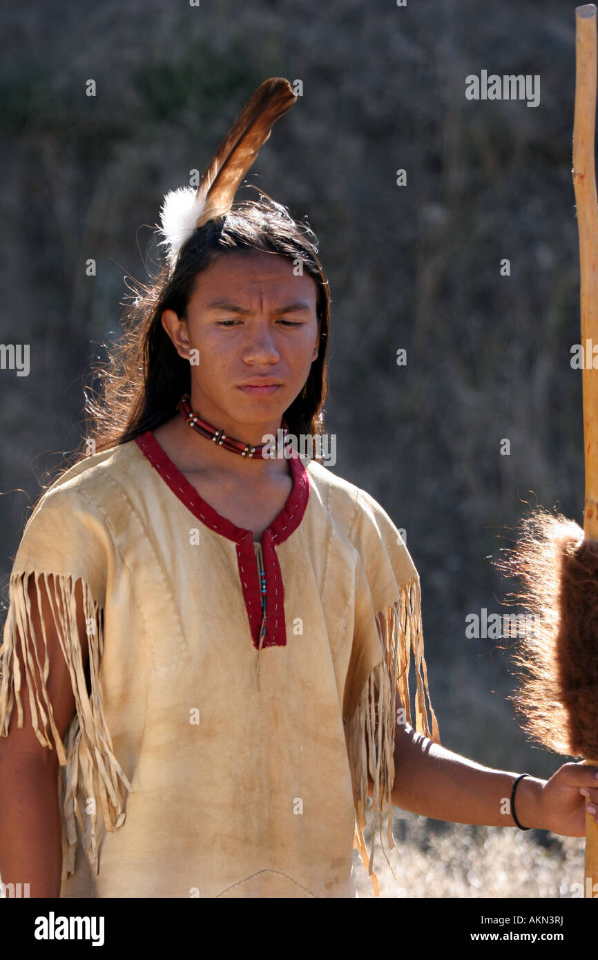 Un Native American Indian boy indossando una piuma in piedi accanto a un cavallo tenendo un colpo di bastone con pelle di bufalo su di esso Foto Stock