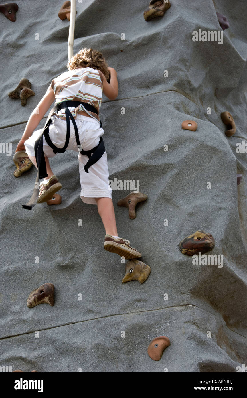 Ragazzo giovane salendo un modello di parete di roccia che indossa una imbracatura di sicurezza adottate in verticale con una copia dello spazio sul fondo Foto Stock