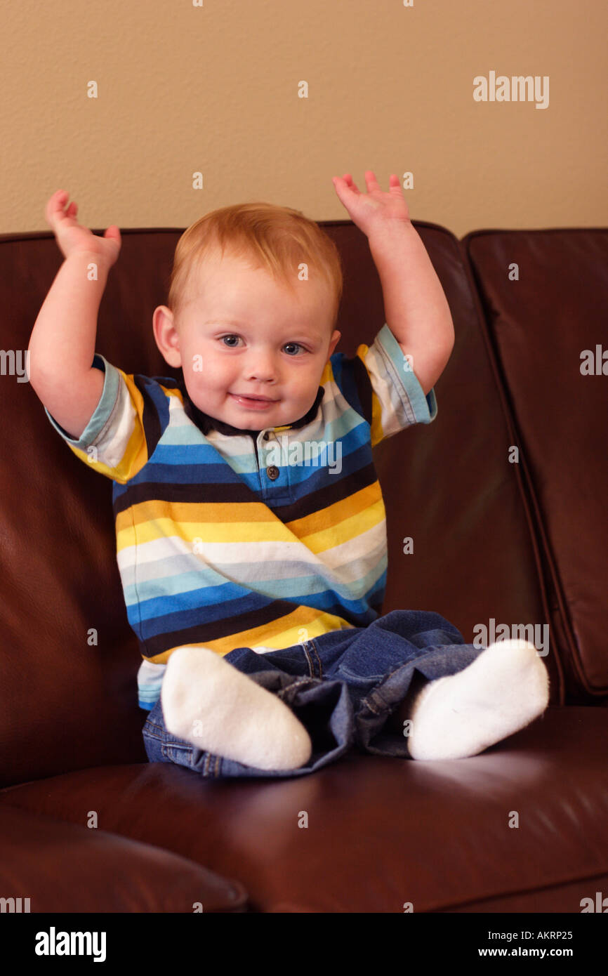 Bambino seduto sul divano con le braccia in alto Foto Stock