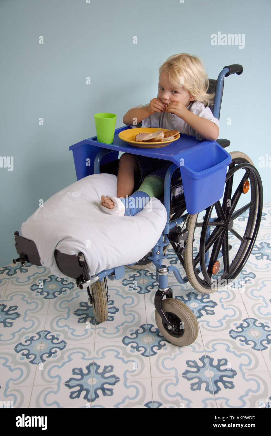 Ragazzino con una gamba rotta avente un pasto in una sedia a rotelle Foto Stock