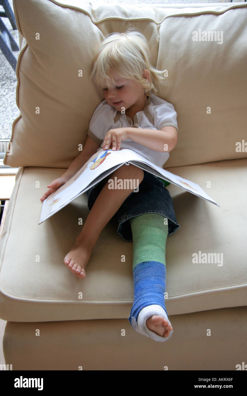 Ragazzino con una gamba rotta la lettura di un libro Foto Stock