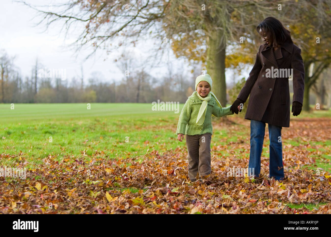 Un giovane razza mista ragazza camminare attraverso le foglie di autunno con sua madre Foto Stock