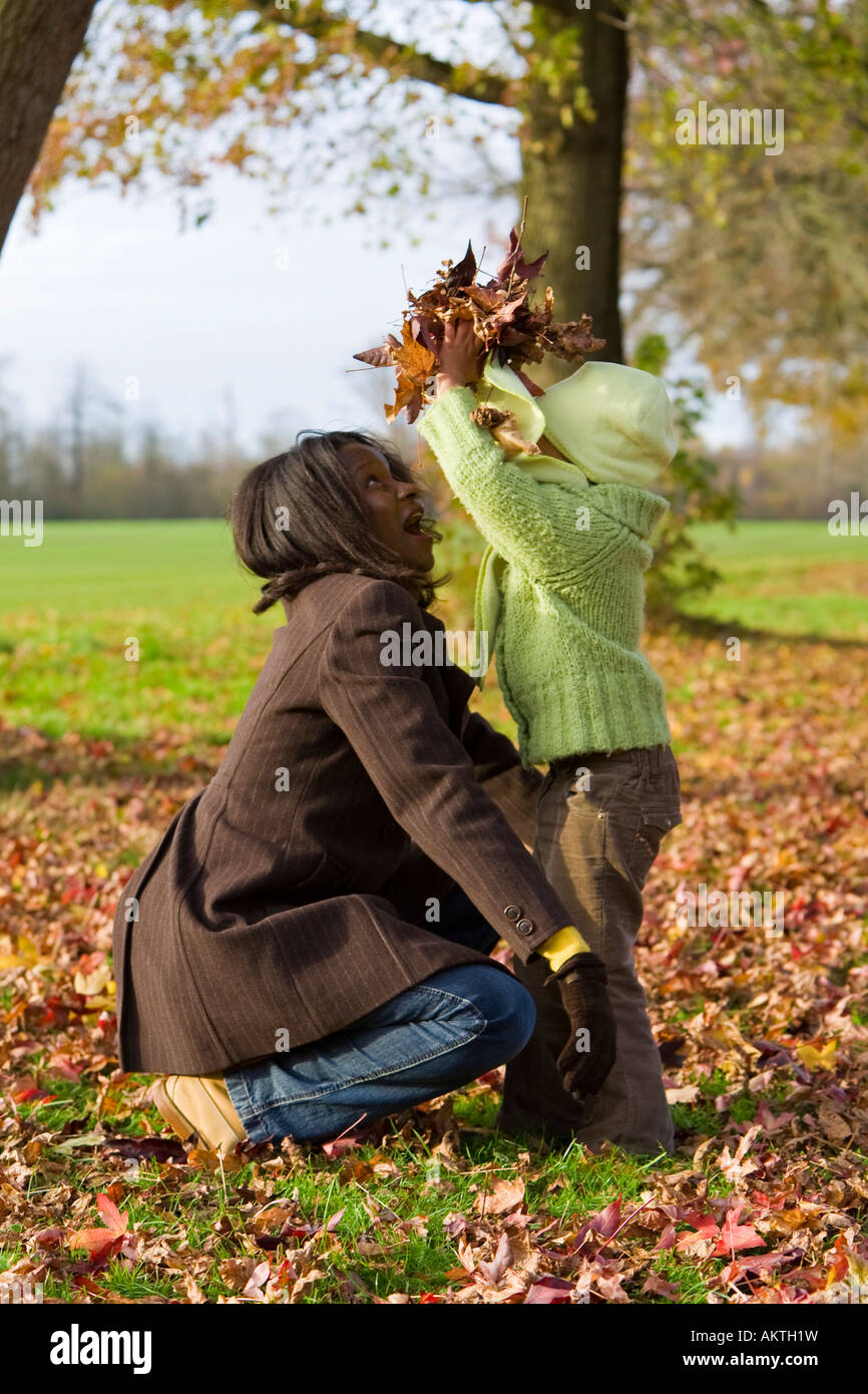 Un giovane razza mista ragazza che gioca in foglie di autunno con sua madre Foto Stock