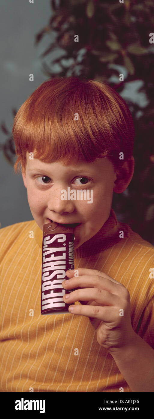 Giovani freckle freckled face red head intitolata boy 5 6 7 mangiare Hershey Chocolate candy bar Foto Stock