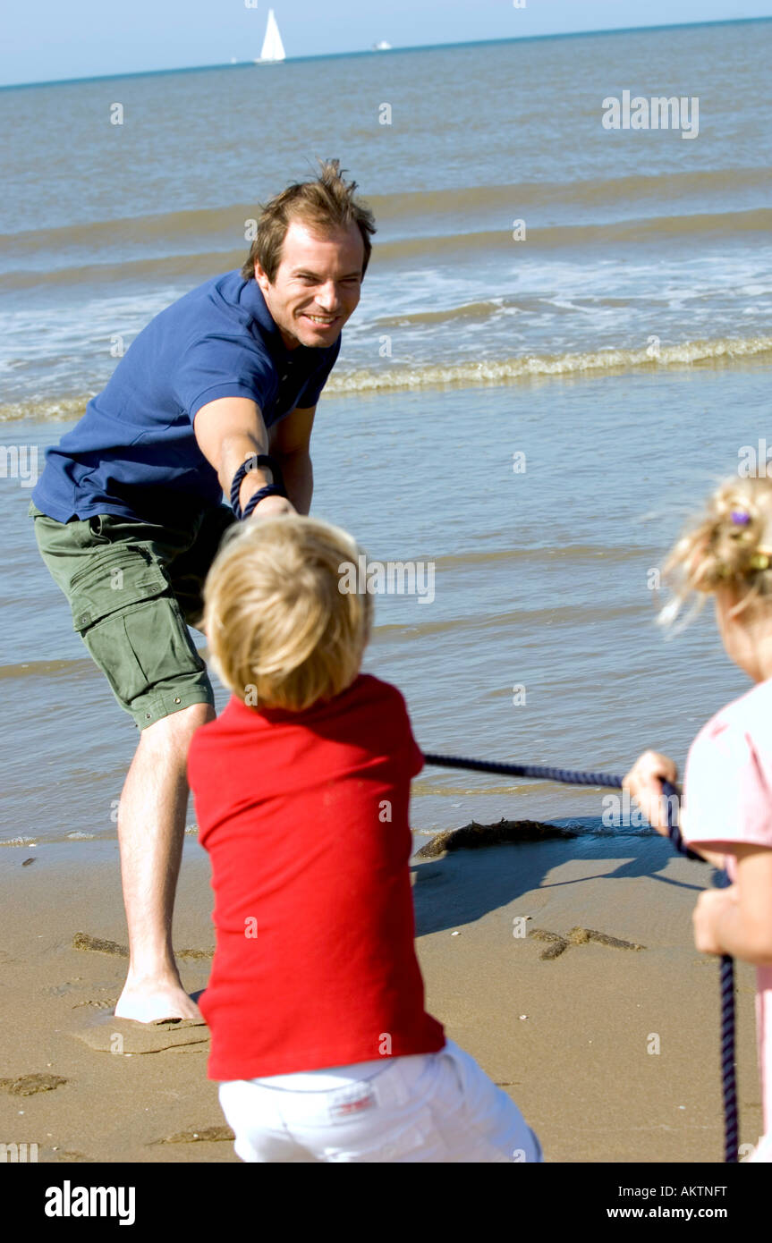 Padre giocando rimorchiatore di guerra con i bambini sulla spiaggia Foto Stock
