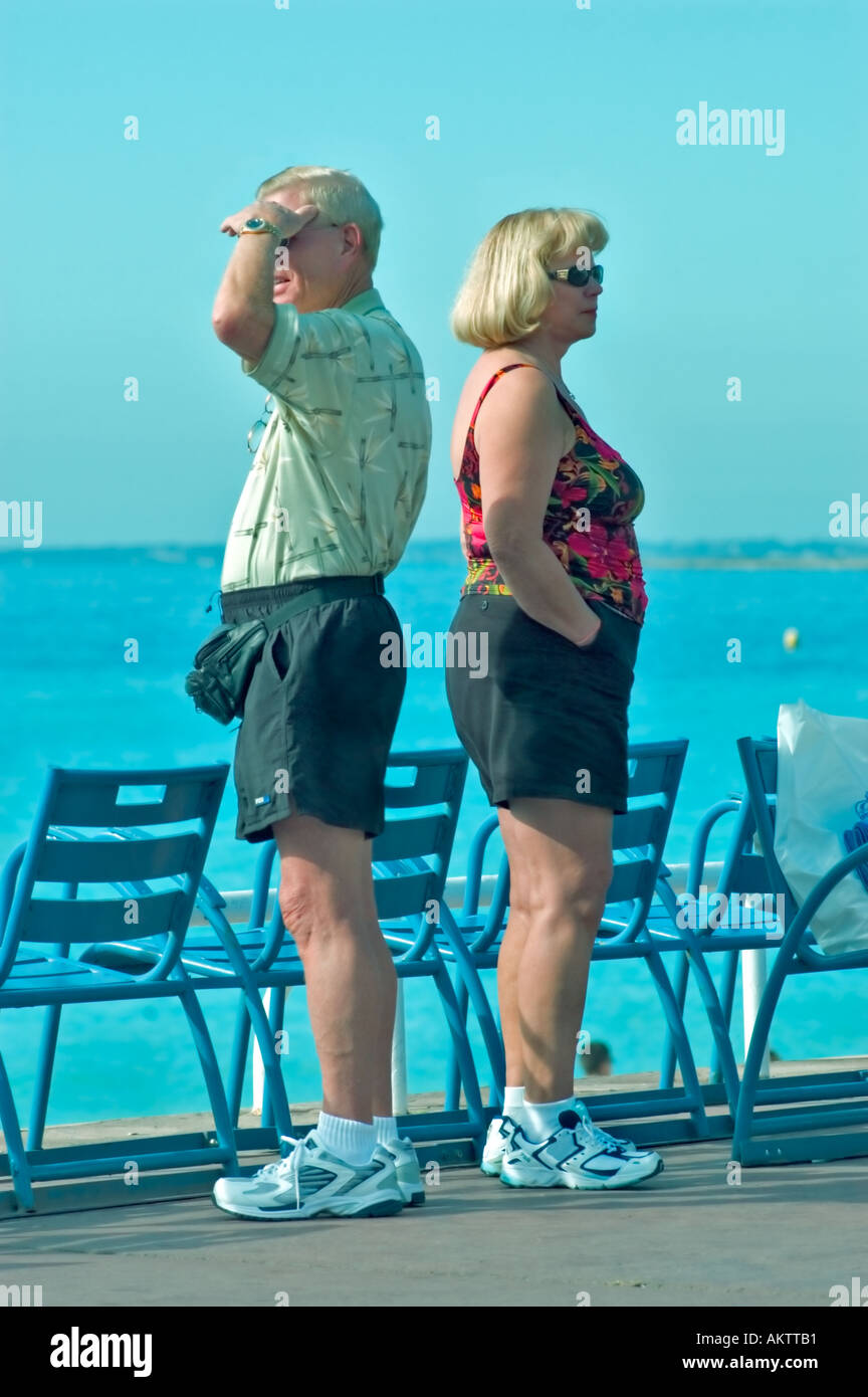 Nizza Francia, scena di spiaggia coppia di mezza età vicino all'acqua in pantaloncini e scarpe da ginnastica in piedi 'Back to Back' in Profile on Vacation, donna della costa azzurra Foto Stock