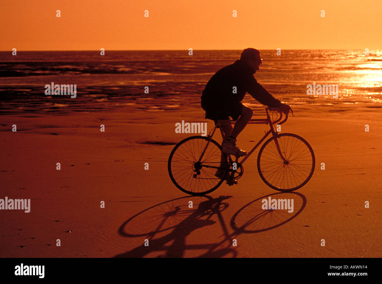 L'uomo maschio in sella per bicicletta bici tra la sabbia spiaggia tramonto mostra mare oceano in background Foto Stock