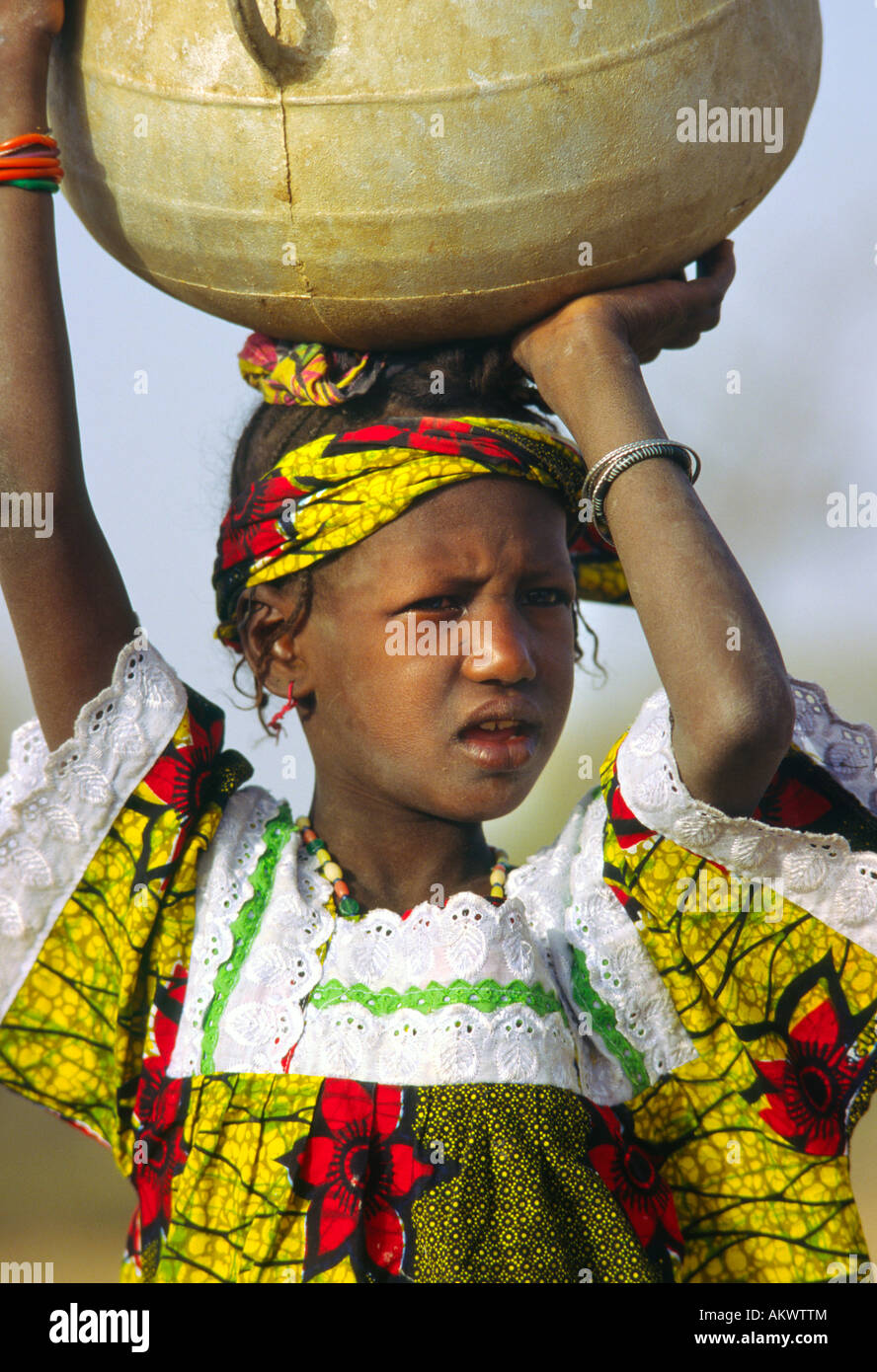 Ragazza Dogon equilibra una grande pentola di metallo sul suo capo Foto Stock